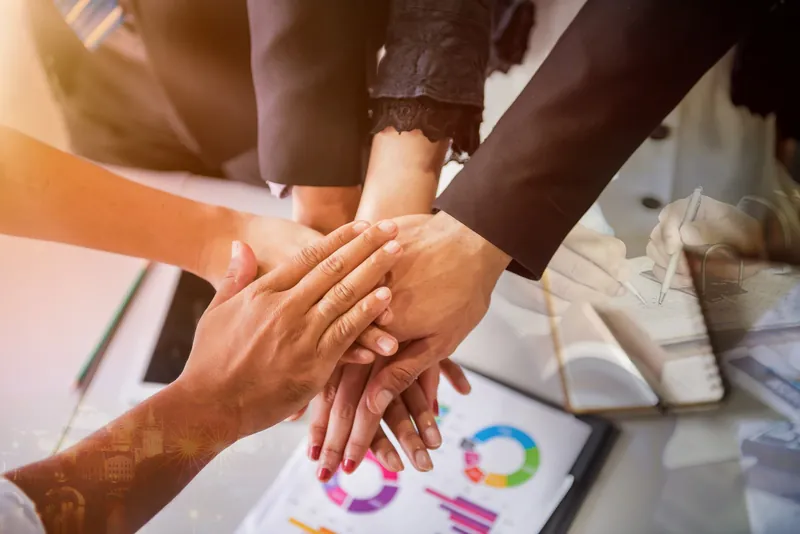 Team stacking hands together over a desk